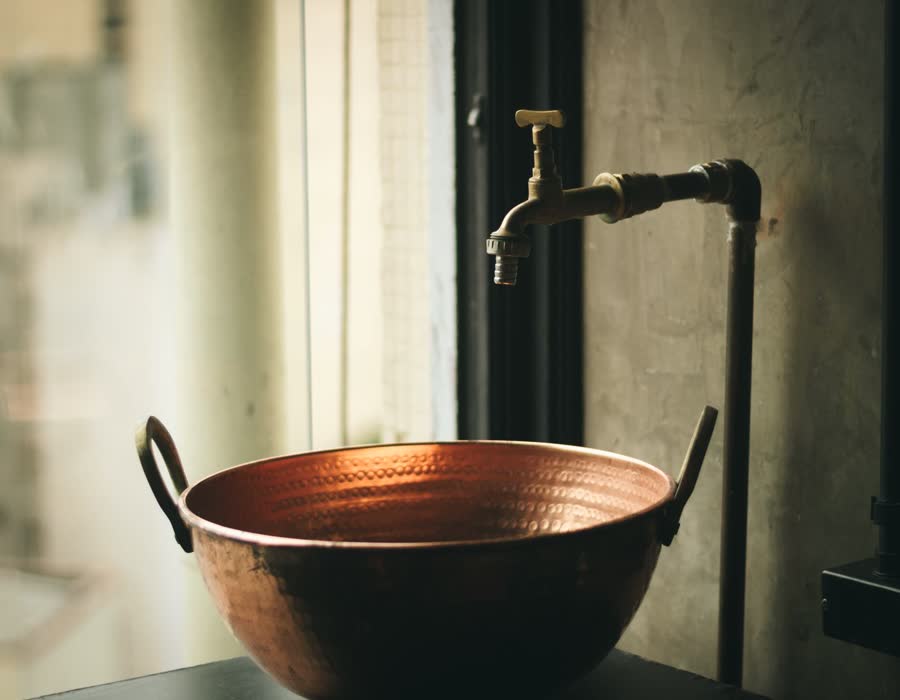 A running tap over a copper basin in low light